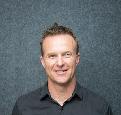 Headshot of a man in a black shirt behind a grey background. 
