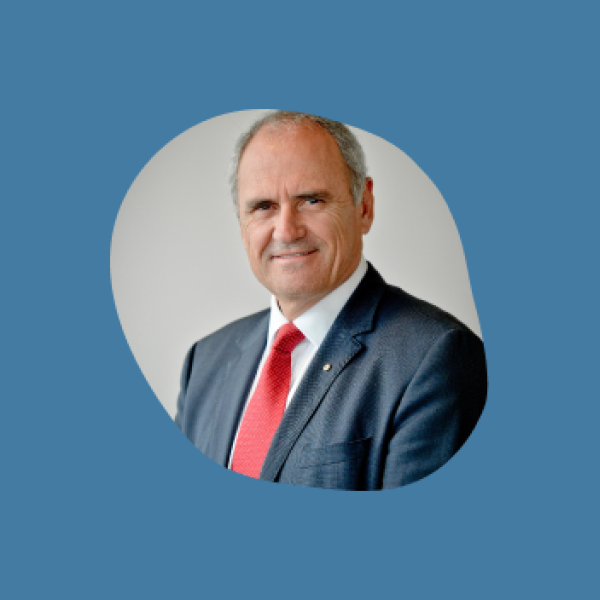 A photo of a man in a blazer and red tie inside an organic pebble shape. It sits on a blue background.