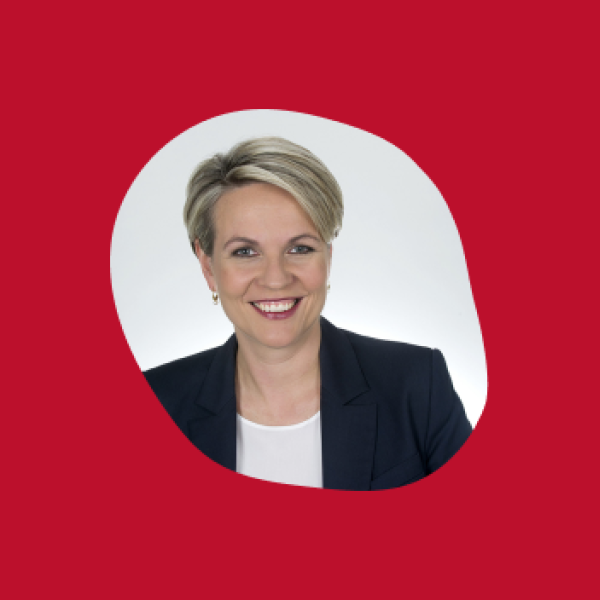 Photo of a woman with a blonde short haircut and blazer inside an organic shaped pebble. It sits on a red background.