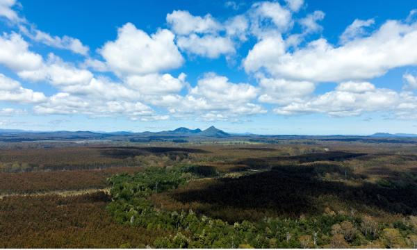 Blue sky with clouds, mountains in the distance and greenery in the foreground.