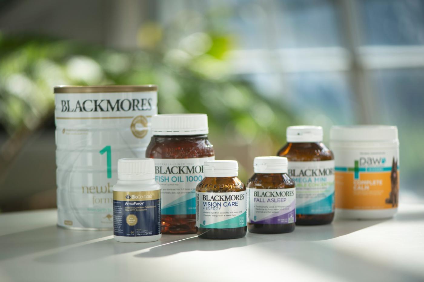 Seven Blackmores bottles of vitamins and baby formula sit on a white table.